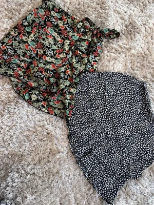 Två blommiga omlottkjolar - Säljer två korta omlottkjolar med blommigt mönster. Den ena är mörkblå med små vita blommor och den andra har en svart botten med färgglada blommor i rött, grönt och blått samt knytband i midjan. Perfekta för en trendig och somrig look. Den blå kjolen med vita blommor är från Lindex, Holly&white, i storlek XS. Den färgglada blommiga kjolen med omlott knyt är från Only i storlek XS