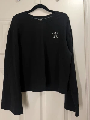 Svart Calvin Klein sweatshirt - Svart sweatshirt från Calvin Klein med CK-logga på bröstet. Tröjan har rund hals och breda långa armar. Loggan är hel men syns att tröjan är använd, i gott skick!