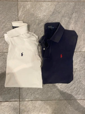 Pikétröjor från Polo Ralph Lauren - Två klassiska pikétröjor från Polo Ralph Lauren, en vit och en marinblå. Båda har den ikoniska broderade loggan på bröstet och krage med knappar. Slim fit-modell i mjuk bomull som passar perfekt till jeans eller chinos.