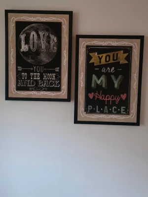 Två tavlor med textmotiv - Säljer två tavlor med inspirerande textmotiv i svart, beige och färgglada detaljer. Ena tavlan har texten 'Love you to the moon and back' med en måne, och den andra 'You are my happy place' med hjärtan. Perfekta som väggdekoration i hemmet.