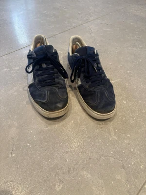 Valentino flycrews  - Snygga mörkblå sneakers från Valentino med vita detaljer på sidan och vit sula. Skorna har klassisk låg modell och är tillverkade i mocka och läder. Perfekta för dig som gillar stilrena och exklusiva sneakers med en sportig touch.