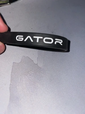 Svart gator armband - Snyggt svart silikonarmband från Gator med vit text där det står 'GATOR' och 'PERFORM MORE'. Perfekt accessoar för dig som gillar sportig och enkel stil. Armbandet är flexibelt och bekvämt att bära hela dagen.