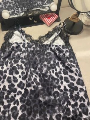 Leopardmönstrat nattlinne med spets - Säljer ett nattlinne med leopardmönster i svart och grått. Nattlinnet har tunna justerbara axelband och dekorativ svart spets längs halsringningen och axlarna. Materialet är glansigt och mjukt, perfekt för att chilla hemma.