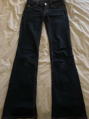 Cheap monday jeans - Säljer ett par mörkblå bootcut jeans med klassiska kontrastsömmar och femficksdesign. Jeansen har en låg midja och är tillverkade i denim med stretch för extra komfort. Perfekt för dig som gillar en tidlös och snygg look.