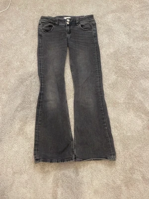 Svarta bootcut jeans Gina Tricot - Snygga svarta bootcut jeans från Gina Tricot med klassisk femficksmodell och knappgylf. Jeansen har en lätt tvättad look och är tillverkade i mjukt denimtyg som ger en bekväm passform. Perfekta för dig som gillar en retroinspirerad stil.