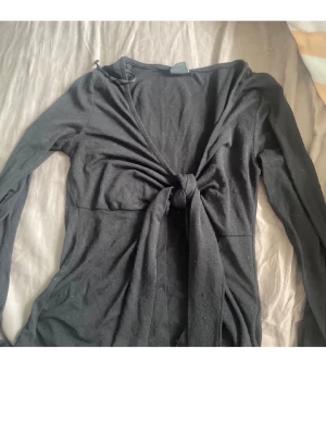 Svart långärmad topp Gina Tricot - Snygg svart långärmad topp från Gina Tricot med knyt framtill. Toppen har en figurnära passform och är tillverkad i mjukt material som känns skönt mot huden. Perfekt att styla med jeans eller kjol för en trendig look.