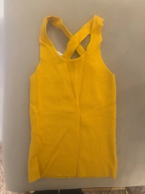 Gul ribbad linnetopp från Mango - Superfin gul ribbad linnetopp från Mango med breda axelband som korsas i ryggen. Toppen är ärmlös och har en tight passform, perfekt för att lyfta vilken outfit som helst. Materialet känns mjukt och stretchigt.