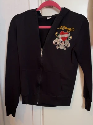 Ed Hardy zipper - Svart ziphoodie från Ed Hardy i strl L. Hoodien har tryck fram och bak med stenar samt tryck på luvan. 