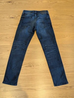 Jack & Jones jeans - Säljer ett par snygga mörkblå jeans från Jack & Jones i modellen "comfort mike". Jeansen är i storlek 28/32. Byxorna är aldrig använda och i superbra skick! Skriv gärna vid funderingar och frågor!.