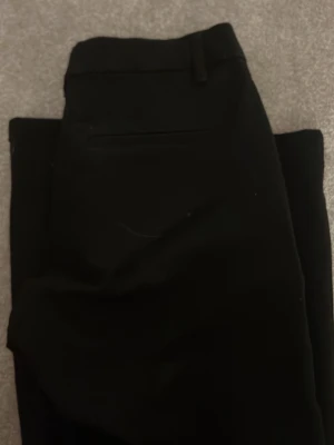 Svarta kostymbyxor från Lindex - Snygga svarta kostymbyxor från Lindex i storlek 164. Klassisk rak passform med bälteshällor och diskret bakficka. Perfekta för en stilren look och passar till skjorta eller kavaj.