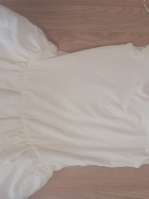 Vit kortklänning med volang - Söt vit kortklänning med volangkant nedtill och enkel, rak passform. Klänningen har en mjuk och luftig känsla, perfekt för varma dagar. Passar dig som gillar en stilren och fräsch look.