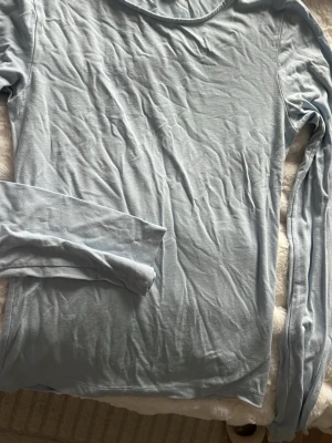 Ljusblå långärmad topp - En enkel och stilren ljusblå långärmad topp i mjukt material. Perfekt att matcha med jeans eller kjol för en clean look. Toppen har rund halsringning och en smal passform.