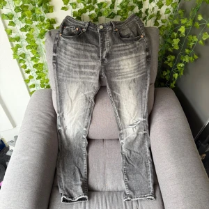 Grå slitna jeans - Säljer ett par grå jeans med slitningar och tvättade detaljer. Jeansen har knappgylf och smal passform. Perfekta för dig som gillar en tuff och avslappnad stil. Tyvär ingen tagg