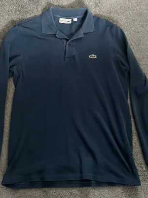 Långärmad Lacoste piké - Säljer en blå långärmad Lacoste piké, sparsamt använd.