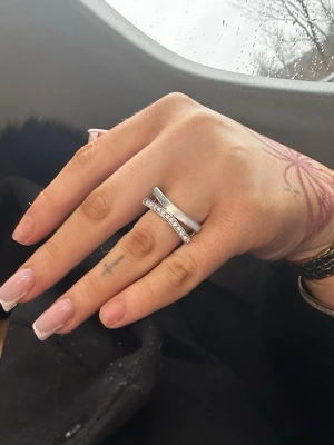 Snygg silverring med stenar - Unik silverfärgad ring i modern design med två parallella band, varav det ena är dekorerat med gnistrande stenar. Ringen har en stilren och trendig look som passar perfekt för dig som gillar minimalistiska accessoarer.