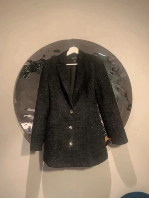 Svart glittrig kavaj med kristallknappar - Snygg svart kavaj klänning från boohoo  med glittriga detaljer och tre kristallknappar framtill. Kavajen har en rak passform, klassisk krage och är helfodrad. Perfekt för dig som vill sticka ut med en elegant och trendig look.