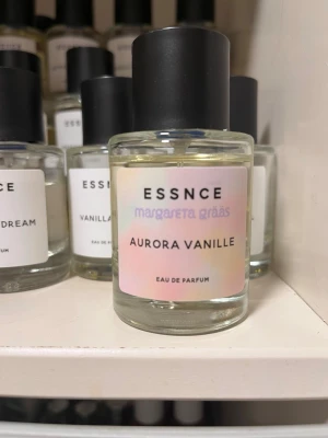 Aurora Vanille parfym från Essnce - Aurora Vanille från Essnce är en Eau de Parfum i en rund glasflaska med svart lock. Etiketten har en mjuk pastellfärgad ton och tydlig text. Doften har inslag av vanilj och flaskan har en stilren, minimalistisk design som passar perfekt på parfymhyllan.