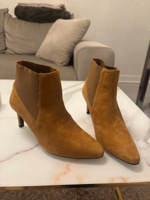 Bruna stövletter med smal klack - Snygga bruna stövletter i mockaimitation med smal klack och spetsig tå. Resårdetaljer på sidorna för enkel påtagning och en trendig look. Perfekta för dig som vill ha en stilren och modern sko till hösten.