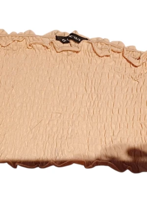 Beige smockad tubtopp från SOC - Säljer en beige smockad tubtopp från SOC. Toppen är axelbandslös med vågig kant upptill och nedtill, och har en stretchig, rynkad struktur som sitter snyggt på kroppen. Perfekt att matcha med höga jeans eller kjol.