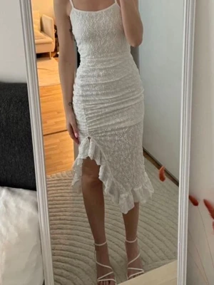 Vit spetsklänning - Säljer en vit, figurnära klänning med smala axelband och vacker spets. Klänningen har en slits framtill med volangkant som ger en extra touch. Perfekt för sommarens alla tillfällen. Materialet känns lätt och luftigt. Har använt endast 1 gång, inga skador 