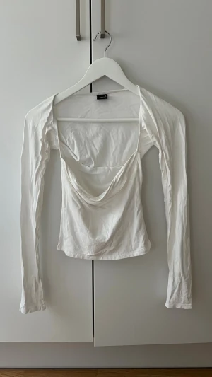 Vit långärmad topp med drapering - Trendig vit långärmad topp från Bershka med snygg drapering framtill och croppad passform. Tillverkad i mjuk bomullsmix som känns skön mot huden. Perfekt att styla med jeans eller kjol för en cool look.