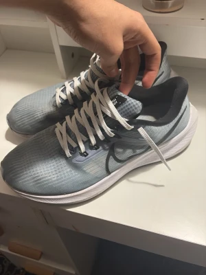 Nike ljusgrå sneakers med svart swoosh - Nike sneakers i ljusgrå mesh med vit sula och svart swoosh på sidan. Skorna har vita snören och svart vadderad häl. Lätta och sportiga med modern design, perfekta för dig som gillar streetwear och sportig stil.