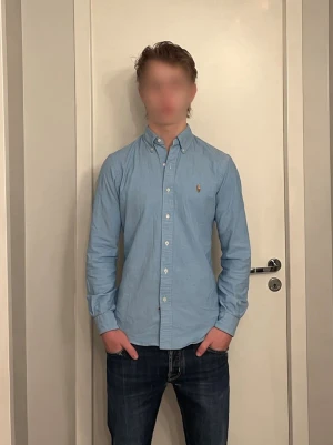 Ljusblå skjorta från Polo Ralph Lauren - Säljer en ljusblå skjorta från Polo Ralph Lauren, skjortan är slim-fit. Skjortan är tillverkad i bomull, har långa ärmar och knappar framtill. Perfekt för dig som gillar stilrena och tidlösa plagg. Nypris ca 1500, storlek S funkar för M. Hör av er vid funderingar!