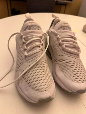 Nike Air Max 270 vita sneakers - Nike Air Max 270 sneakers i vitt med ljusbeige detaljer och genomskinlig Air Max-sula. Ovandelen är i mesh och syntetmaterial för bra andningsförmåga. Klassisk Nike-logga på sidan och tungan. Snygg och sportig design med lågt skaft.