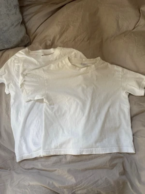 Två vita basic t-shirts  - Säljer två klassiska vita t-shirts i mjuk bomull. Båda har rund halsringning och korta ärmar, perfekt för en clean och enkel look. Passar dig som gillar basic och stilrent. 