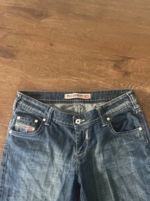 Blå raka jeans från Diesel - Snygga blå jeans från Diesel med klassisk femficksdesign och raka ben. Jeansen har diskreta slitningar och en liten logotyp på myntfickan. Perfekta för en avslappnad och trendig look.