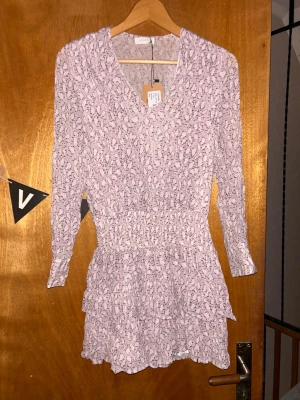 Ljuslila blommig kortklänning - Söt ljuslila kortklänning från Object med blommigt mönster, v-ringning och trekvartsärm. Klänningen har smock i midjan och volangdetaljer på kjolen för en feminin siluett. Perfekt för vår och sommar!