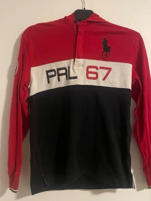 Polo Ralph Lauren PRL 67 hoodie – röd/svart – stl 14/16 - Snygg hoodie från Polo Ralph Lauren med PRL 67 tryck på bröstet och klassiska Polo-loggan. Röd, vit och svart färgkombination med halv zip och huva.  Storlek: 14/16 (passar ungdom / mindre S) Skick: Bra skick  Perfekt till vardags eller streetwear outfit.