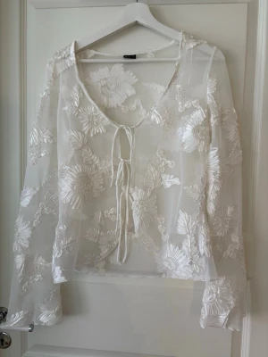 Vit transparent blus med broderi - Säljer en vit transparent blus med långa ärmar och blommiga broderier. Stlr XL men liten i storleken, passar mig som är mellan M och L.