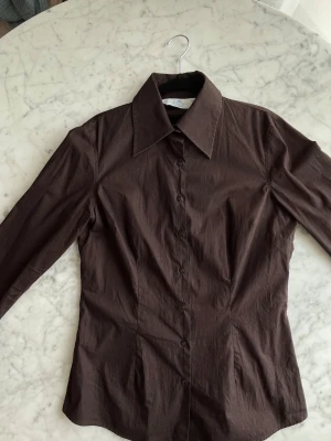 Brun skjorta från Hawes & Curtis - Snygg brun skjorta från Hawes & Curtis. Skjortan har en figurnära passform och långa, lite vidare ärmar. Kameran hade svårt att ta upp färgen men den första bilden är mest lik verkligheten. Skjortan är i fint skick men har tappat lite färg framför allt vid kragen, syns på bild 2.