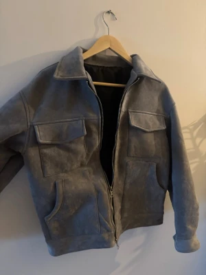 Grå överjacka med fickor - Snygg grå jacka med två stora bröstfickor med lock och två sidofickor. Jackan har dragkedja framtill och klassisk krage. Perfekt för dig som vill ha en stilren och trendig look. Priset går att diskutera.