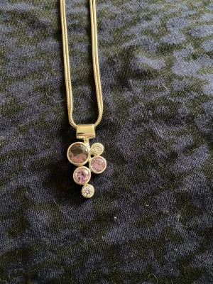 Silverhalsband med lila stenar - Snyggt halsband i äkta silver med ett hänge bestående av fem runda stenar i olika storlekar. Stenarna är lila ametister och klara, infattade i silver. Kedjan är slät och glänsande, vilket ger ett stilrent intryck.