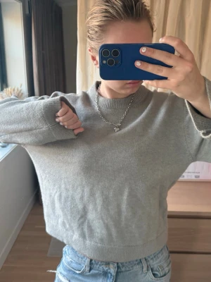 Grå stickad tröja med rund hals - En grå stickad tröja med rund hals och ribbade muddar. Tröjan har en avslappnad, lite loose passform och är långärmad. Materialet ser ut att vara mjukt och behagligt, perfekt att matcha med jeans. Inget synligt märke.