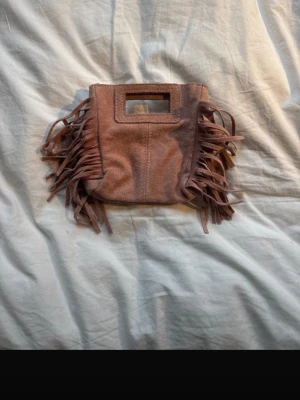 Rosa miniväska med fransar Maje liknande  - Säljer en riosa miniväska i mockaimitation med rektangulärt handtag och långa fransar på sidorna. Väskan har en cool boho-vibe och är perfekt för dig som vill sticka ut. Ingen synlig logga eller märke på utsidan. Maje liknande