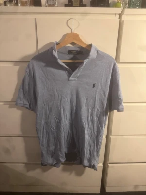 Ljusblå pikétröja från Polo Ralph Lauren - Snygg ljusblå pikétröja från Polo Ralph Lauren med klassisk krage och korta ärmar. Tröjan har den ikoniska broderade loggan på bröstet och är gjord i mjukt bomullsmaterial. Perfekt för en avslappnad och stilren look.