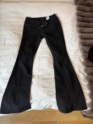 Svarta bootcut jeans med utsvängda ben - Säljer ett par svarta bootcut jeans med riktigt utsvängda ben och klassiska fem fickor. Jeansen har låg midja och är tillverkade i denim med lite stretch. Perfekta för dig som gillar retrostil och vill sticka ut med en cool siluett.