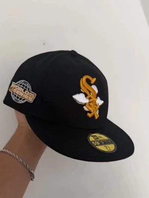 New Era keps - Snygg svart keps från New Era 59FIFTY med gul och vit brodyr framtill och World Series-märke på sidan. Klassisk flat peak och strukturerad passform. Perfekt för dig som gillar sportig streetstyle och vill sticka ut med coola detaljer.