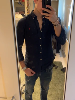 Mörkblå skjorta från Ralph Lauren - Säljer en mörkblå skjorta från Ralph Lauren med klassisk krage och knappar framtill. Skjortan har lång ärm och den ikoniska röda logotypen broderad på bröstet. Perfekt till jeans för en clean och stilren look. Skjortan är inte använd mycket alls. Priser är EJ hugget i sten, hör av dig vid frågor. Med vänlig hälsning