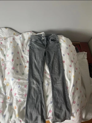 Grå bootcut jeans med låg midja - Snygga grå jeans med bootcut passform och låg midja. Klassisk femficksmodell med dragkedja och knapp framtill. Jeansen har en tvättad look och raka ben som blir lite vidare nedtill. Perfekta för en avslappnad och trendig stil.