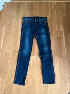 Replay jeans  - Snygga mörkblå jeans från Replay med raka ben och klassiska fem fickor. Jeansen har ljusa slitningar framtill och bakfickor med dekorativa sömmar. Perfekta för en avslappnad och trendig look.