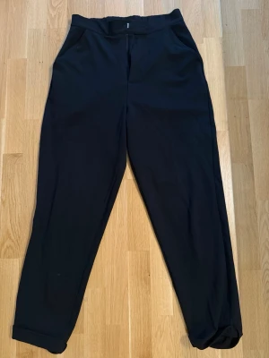 Svarta kostymbyxor med fickor - Stilrena svarta kostymbyxor med klassisk rak passform och diskreta sidfickor. Byxorna har uppvikta benslut och stängs med dragkedja och knapp. Perfekta för en dressad look. Materialet känns mjukt och följsamt.