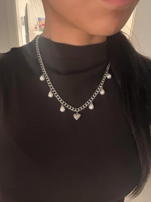 Silvrigt halsband, 6 mm brett med hjärthänge - Matchande örhängen finns i en separat annons. Finns även i guldpläterad variant.  Material: Rostfritt stål Bredd: 6 mm Längd: 42 + 8 cm (justerbar) Övrigt: Nickelfritt och handgjort