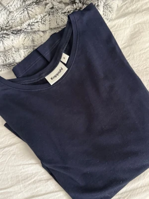 Mörkblå basic tröja från Kappahl - En enkel och stilren mörkblå tröja från Kappahl i mjukt bomullsmaterial. Tröjan har rund halsringning och klassisk passform, perfekt att matcha med jeans eller shorts för en clean look.