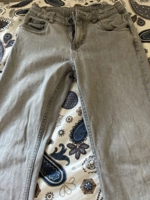 Grå raka jeans med fem fickor - Snygga grå jeans med klassisk femficksmodell och raka ben. Jeansen har bälteshällor och knappgylf. Tillverkade i ett mjukt denimtyg som är skönt att bära. Perfekta för dig som gillar en clean och enkel stil.