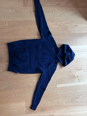 Mörkblå hoodie från Scalpers - Mörkblå hoodie från Scalpers med klassisk huva och dragsnören. Tillverkad i mjukt material och har en stor magficka framtill. Perfekt för en avslappnad och stilren look. Storlek för dig som är runt 160