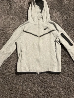 Grå nike tech barnstorlek - Snygg ljusgrå hoodie från Nike med hel dragkedja och svart Nike-logga på bröstet. Huva, två fickor fram och svart detalj på ena ärmen. Pris kan diskuteras!!